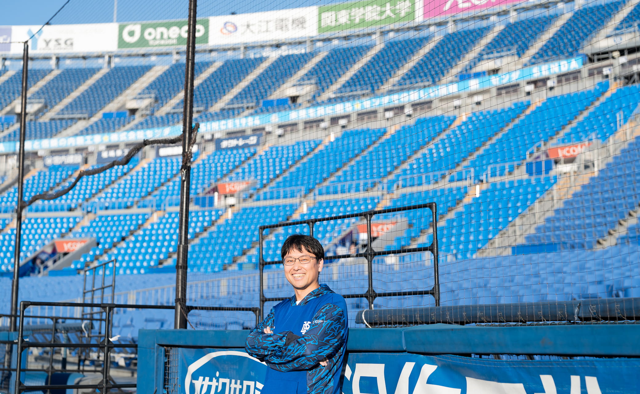 グラウンドのフェンスの前で腕を組む男性